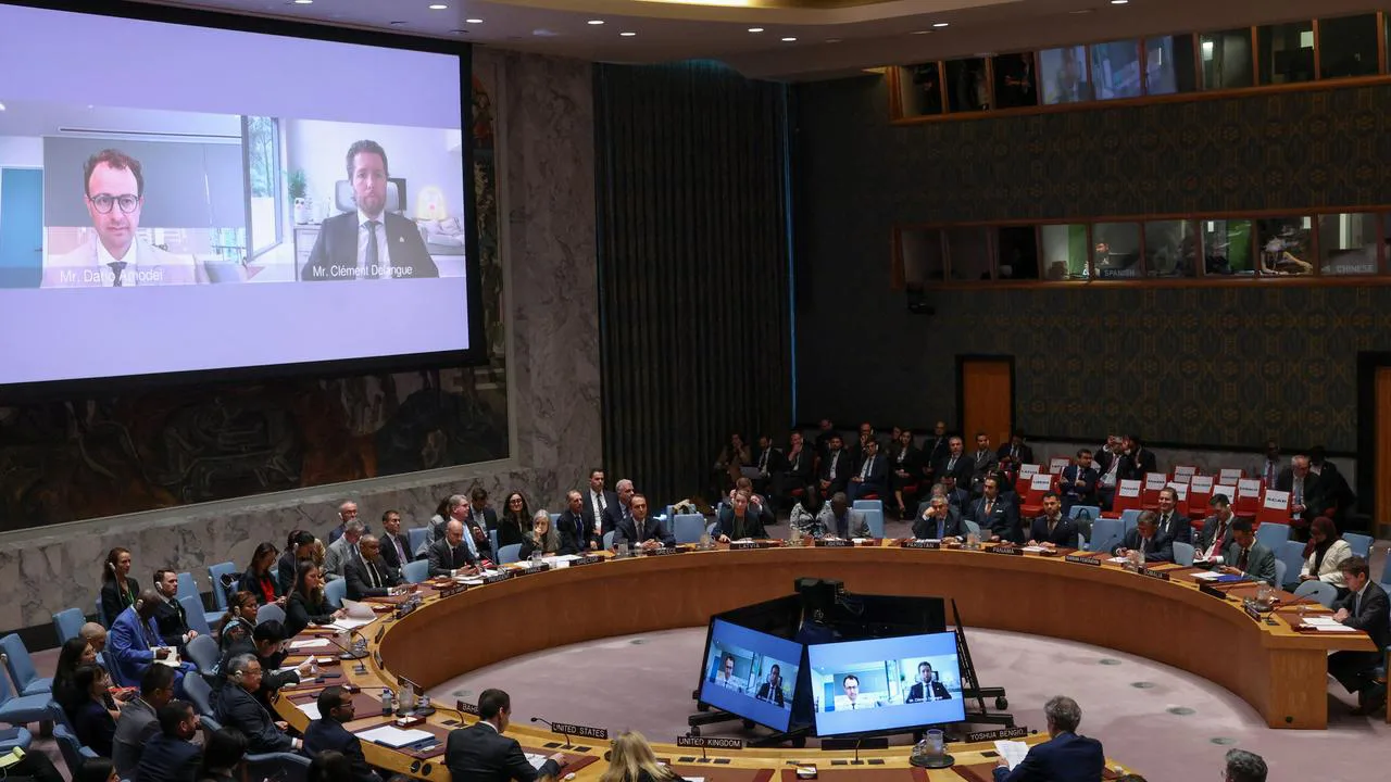 Image of the UN Security Council showing attendees seated on a round table, plus two guests joining online on the screen